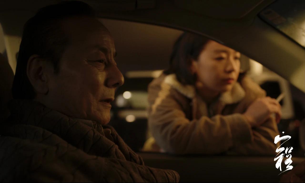 A man sits inside a car while a woman leans beside the open window.