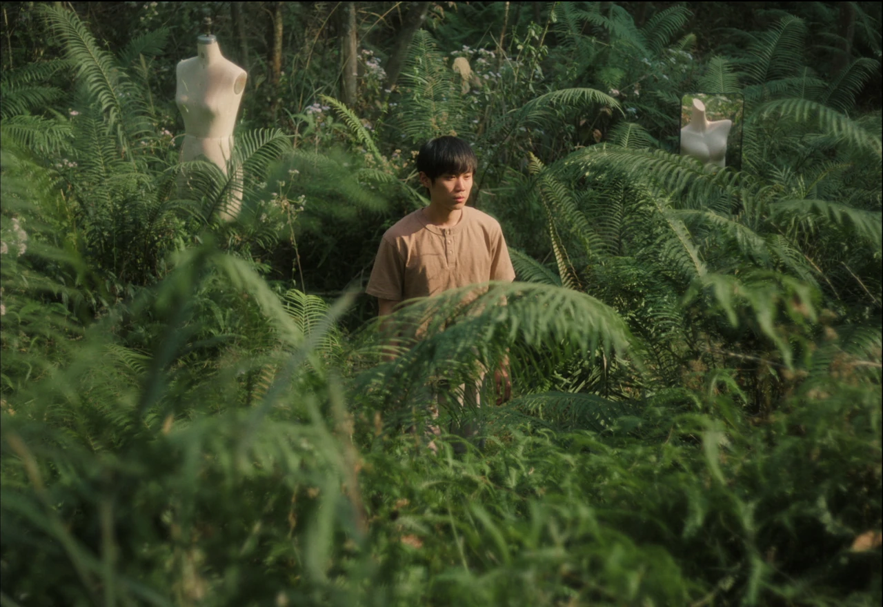 A young person among dense green ferns and dress forms.