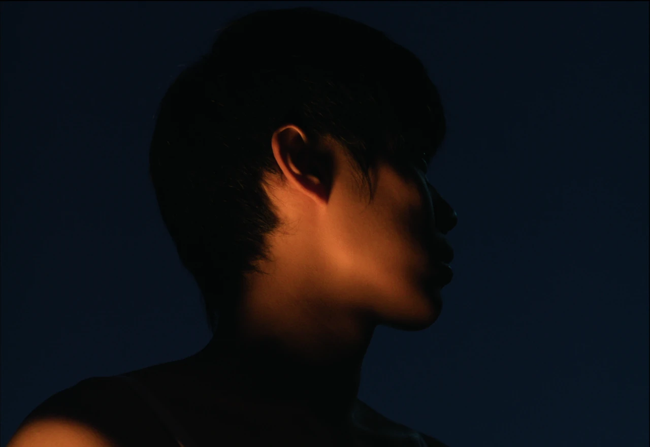 A young person in profile, with warm light across the face against a dark blue background.